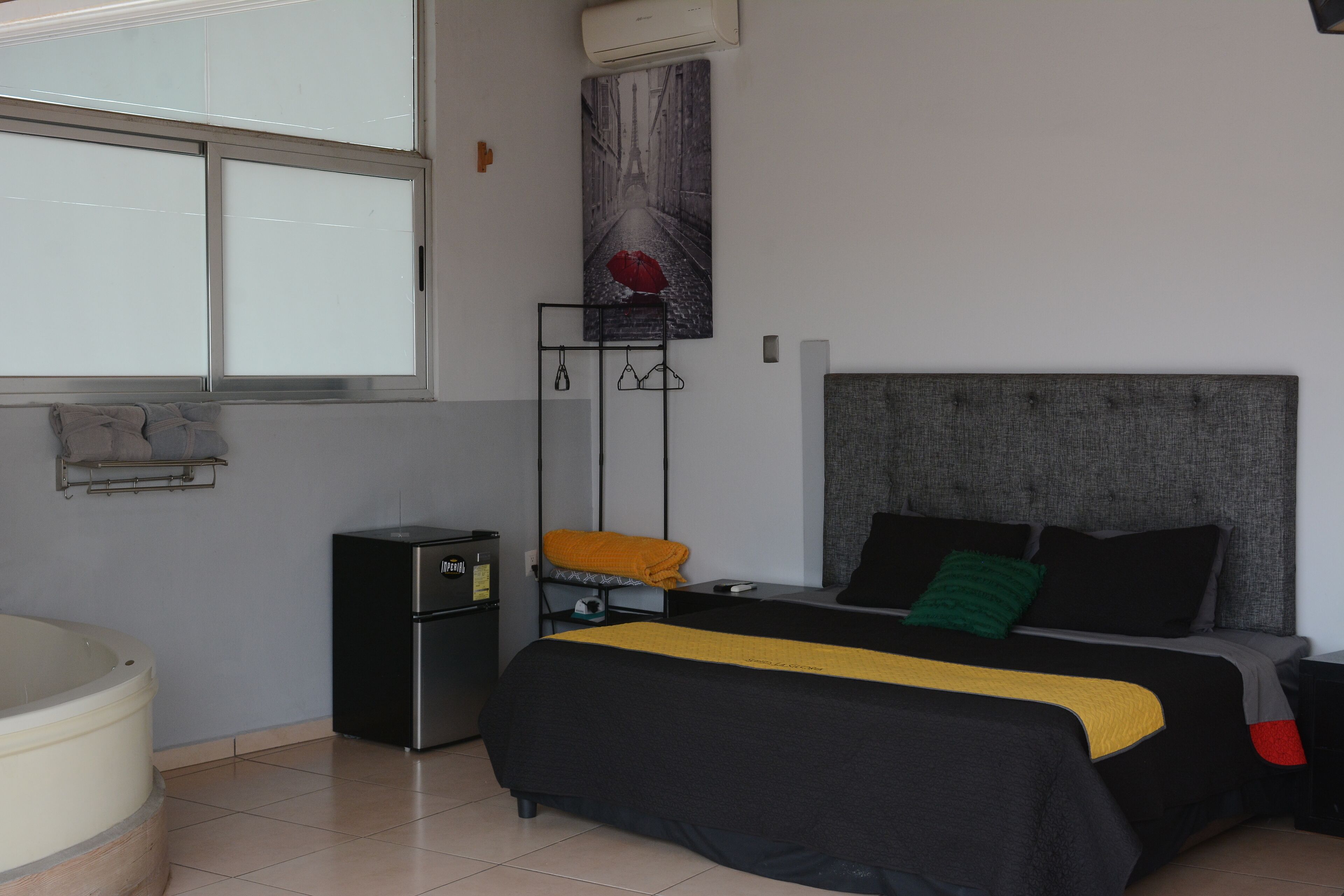 A bedroom with a bed, a small desk, a chair, a heater, and a window.
