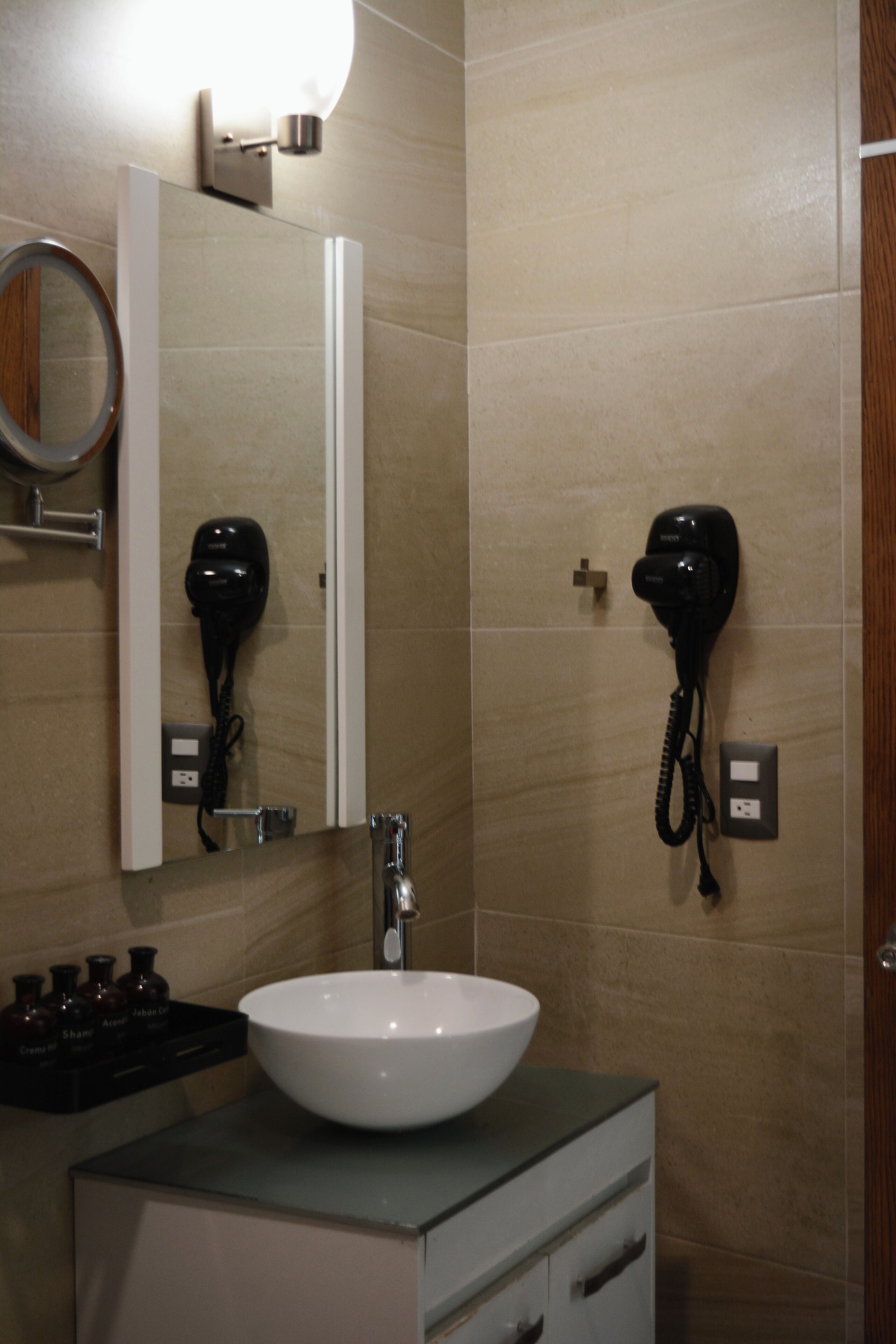 Un baño con un lavamanos blanco, un espejo y dos secadores de pelo fijados en la pared.