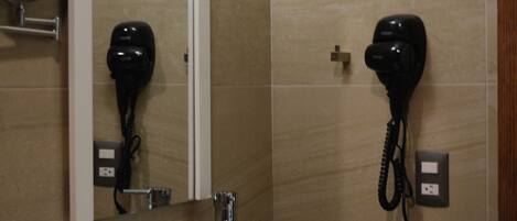 Un baño con un lavamanos blanco, un espejo y dos secadores de pelo fijados en la pared.