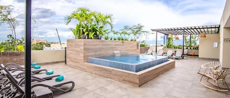 A rooftop pool area with lounge chairs, a hot tub, and potted plants.