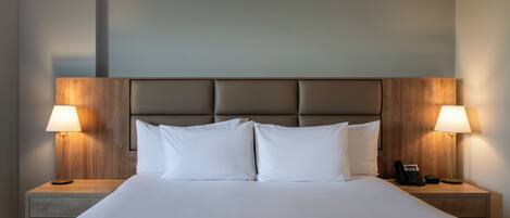 Una cama bien tendida con sábanas blancas, dos lámparas de noche y un teléfono en la mesita.