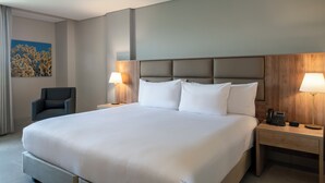 A large bed with white linens, two bedside lamps, a wooden headboard, a nightstand with a phone, and a chair. - Hilton Garden Inn Cali Ciudad Jardin (Cali)
