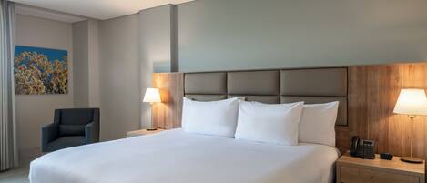 A large bed with white linens, two bedside lamps, a wooden headboard, a nightstand with a phone, and a chair.