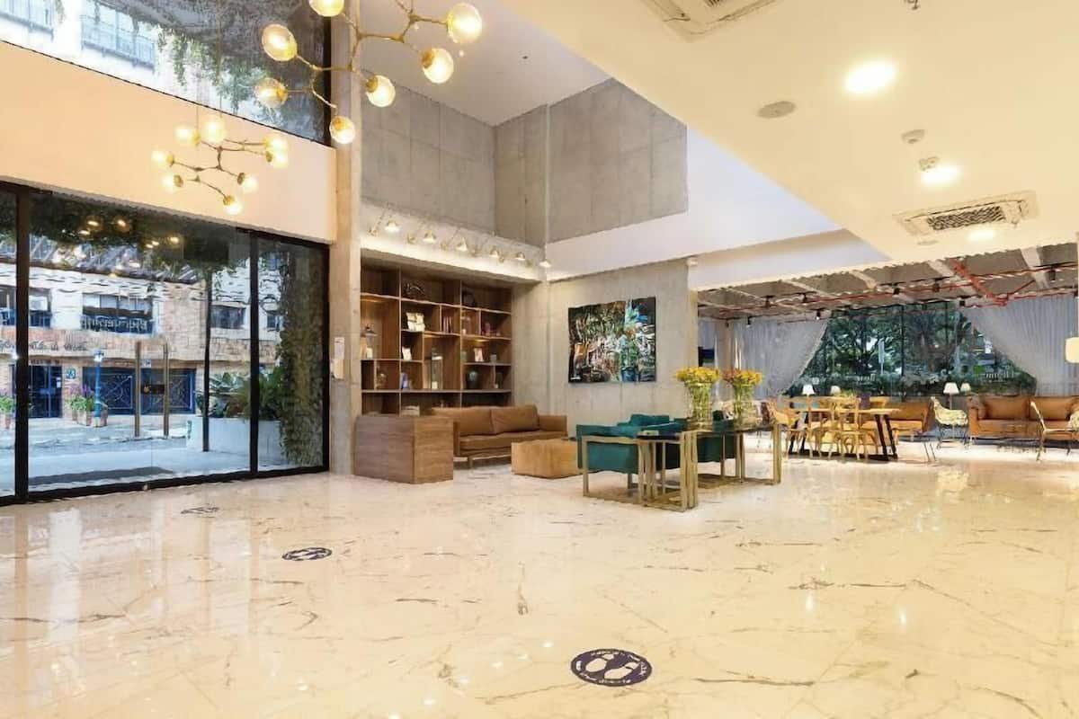 A spacious lobby with a marble floor, a seating area with sofas and tables, a bookshelf, and a large window offering a view of the outside.