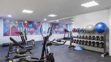 Un gimnasio con equipo de ejercicio, mancuernas y una pared con la marca 'Hilton'.