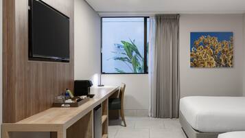 Habitación de hotel con un escritorio de madera, un televisor de pantalla plana, una cama, un ventanal con vistas a plantas y un cuadro de flores.