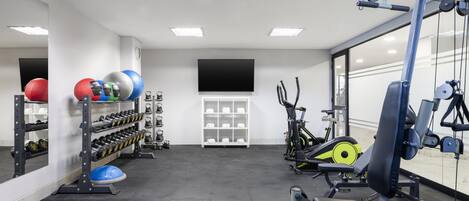 Un gimnasio con equipo de levantamiento de pesas, pelotas de ejercicio y mancuernas.