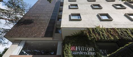 Een Hilton Garden Inn gebouw met een modern ontwerp, bestaande uit een combinatie van glazen en betonnen gevels, en een bord met de naam van het hotel.