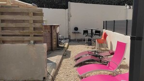 A patio area with outdoor seating, including pink chairs and a table, surrounded by a wooden fence and a white wall.