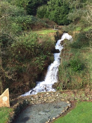 A waterfall cascading over a stone wall into a small pond, surrounded by dense greenery. - Lake View Villa - Rosecraddoc Manor (Liskeard)