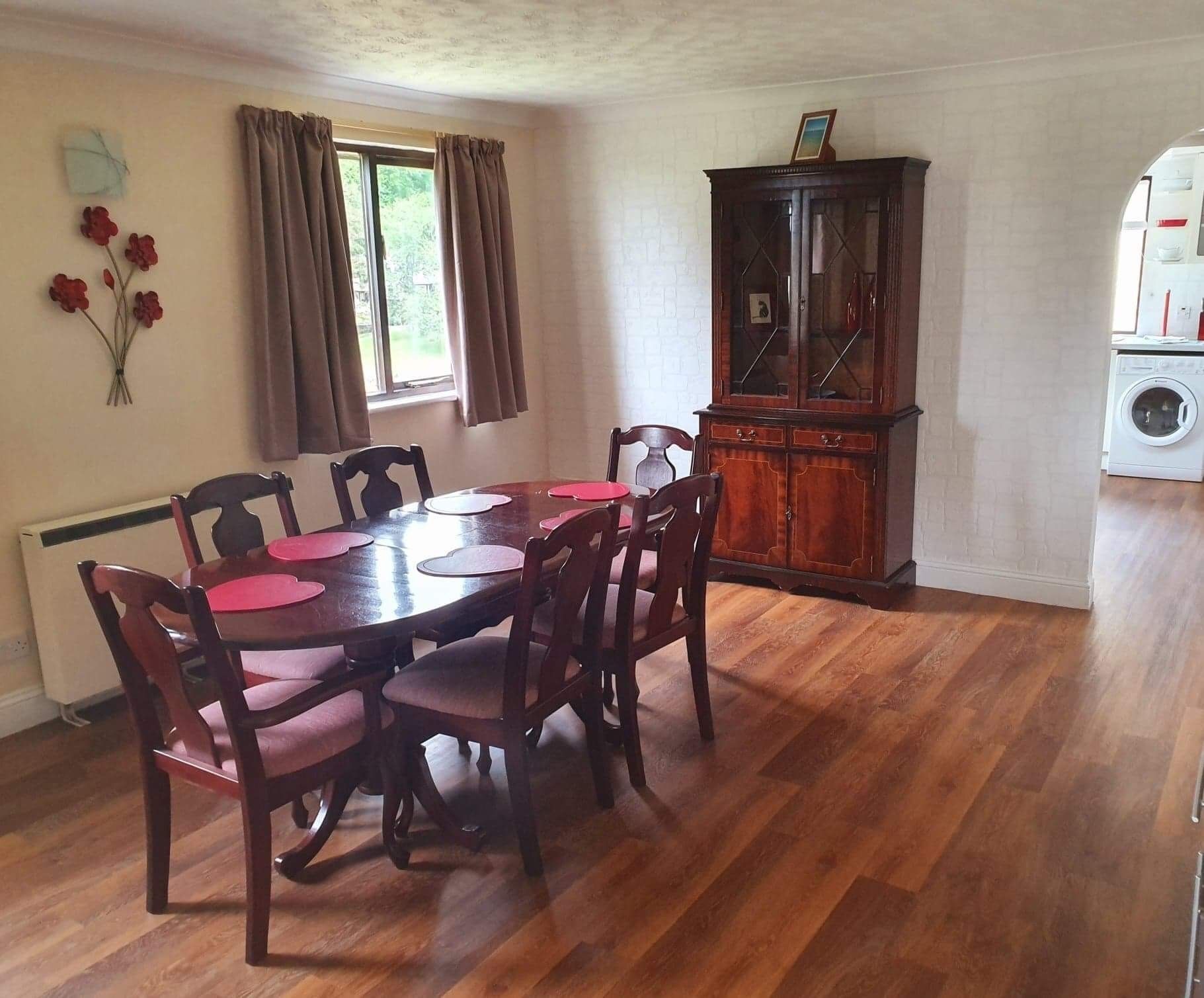 Un coin repas avec une table et des chaises en bois, un buffet et une fenêtre avec des rideaux.