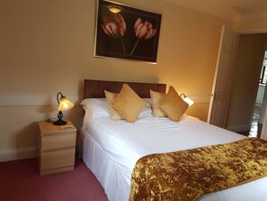 A hotel room with a bed, a nightstand, a lamp, a framed picture of tulips, and a door. - Lake View Villa - Rosecraddoc Manor (Liskeard)