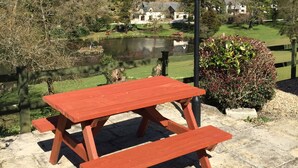 A picnic table with benches in a park setting, surrounded by a pond, trees, and houses in the background. - Lake View Villa - Rosecraddoc Manor (Liskeard)