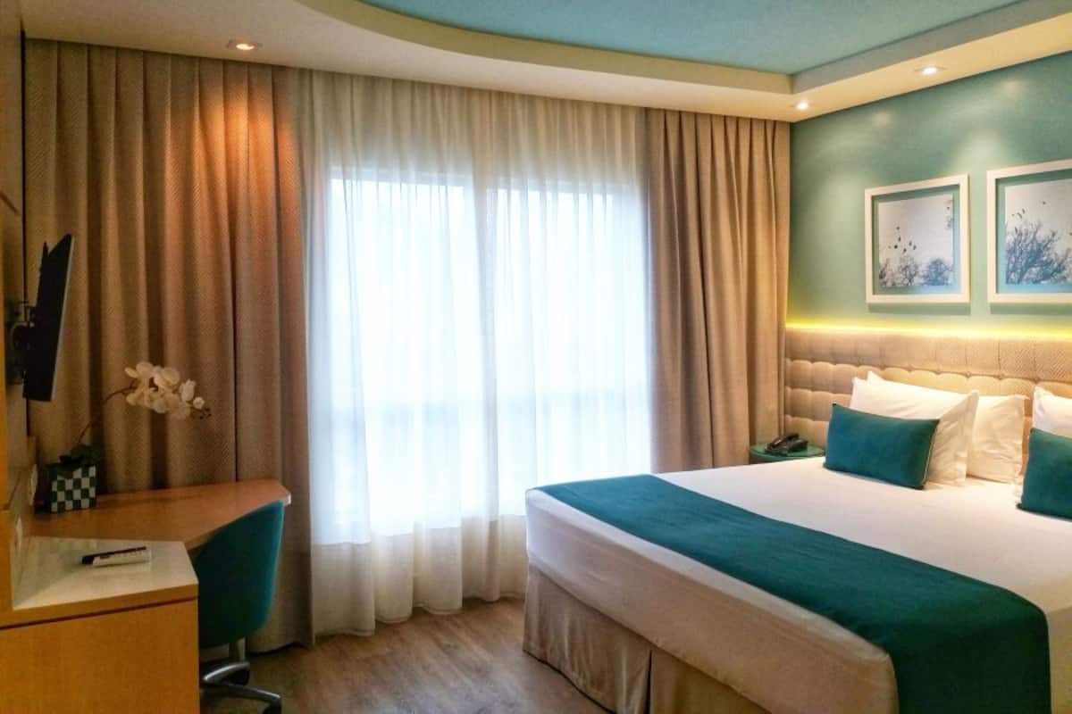 A hotel room with a large bed, a desk, a chair, and a window with curtains.