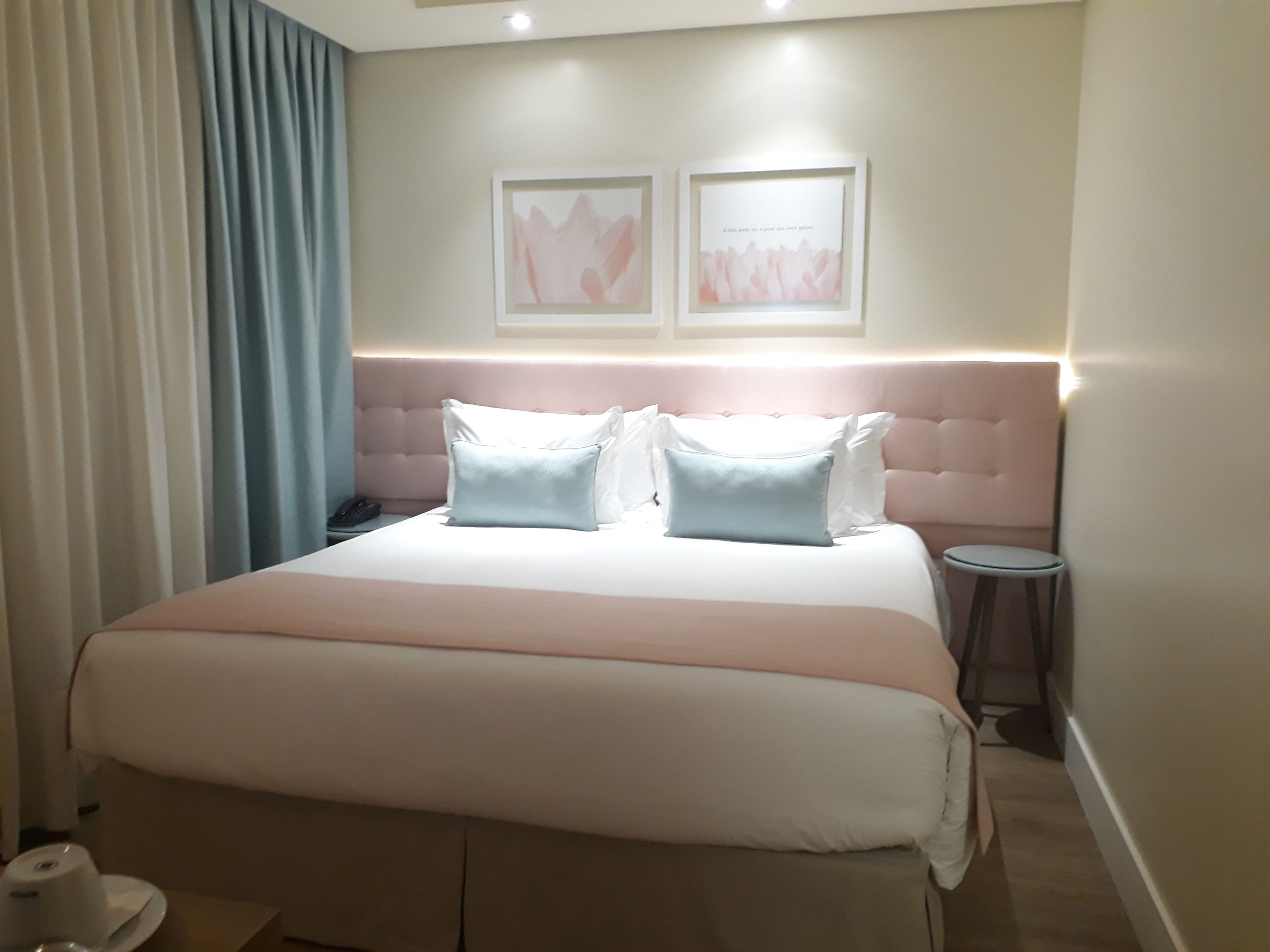 A hotel room with a large bed, a bedside table, a chair, and two framed pictures on the wall.