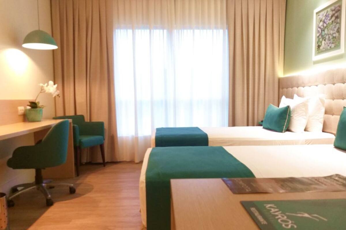 A hotel room with a bed, two chairs, a desk, a lamp, and a window with curtains.
