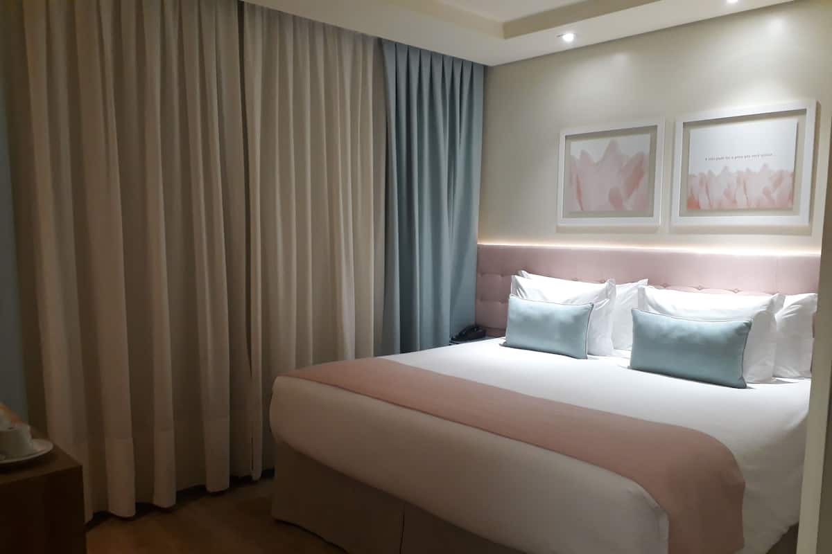 A hotel room with a large bed, a nightstand, and two framed pictures on the wall.