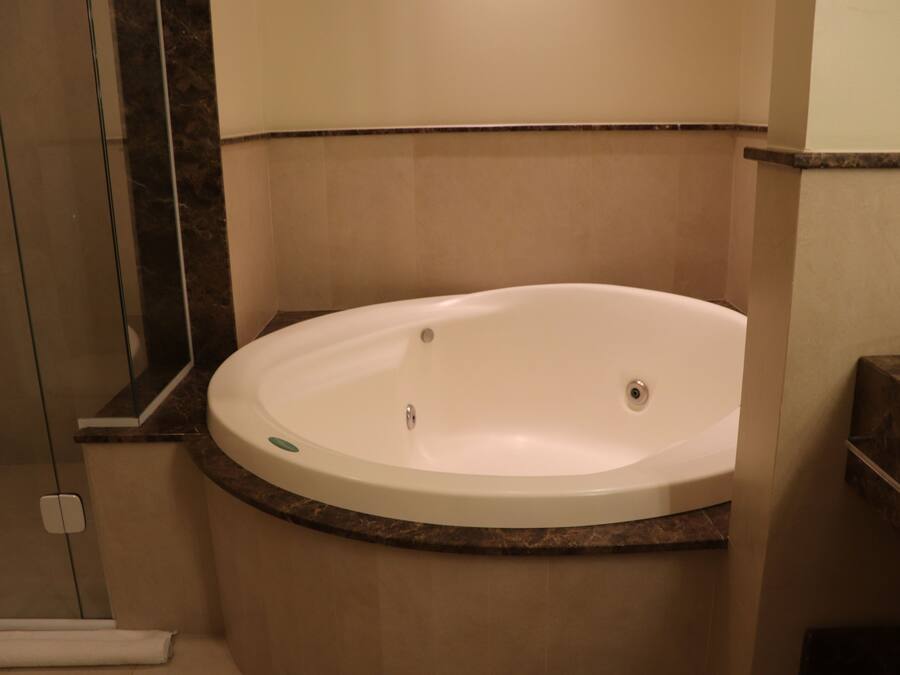 A corner bathroom with a white bathtub, beige tiles, and a marble countertop.