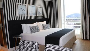 Habitación de hotel con una cama grande, papel tapiz a rayas blanco y negro, y vistas de la ciudad a través de la ventana.