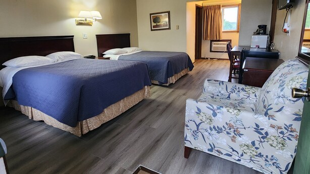 Habitación de hotel con dos camas, un escritorio, una silla, un televisor de pantalla plana y una ventana con cortinas.