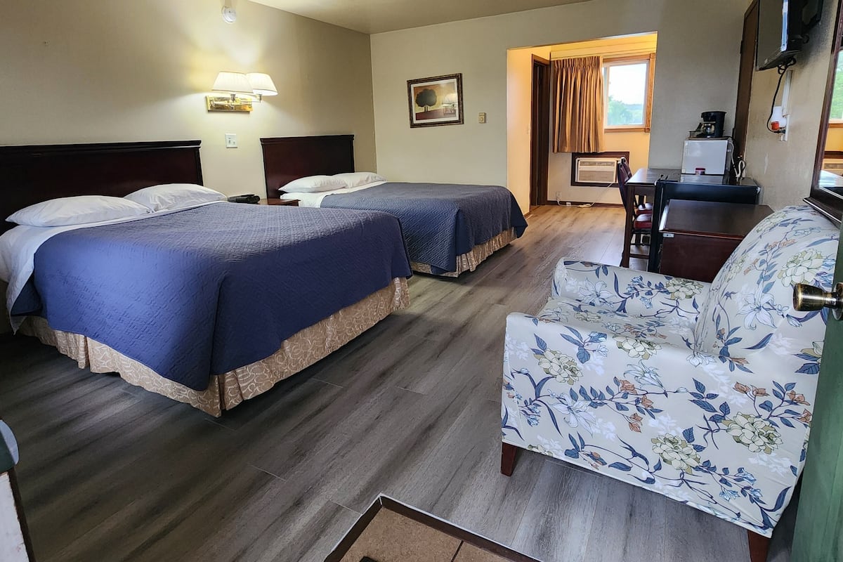 A hotel room with two beds, a desk, a chair, a flat-screen TV, and a window with curtains.