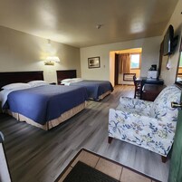 Quarto de hotel com duas camas, uma escrivaninha, uma cadeira, uma televisão de tela plana e uma janela com cortinas.