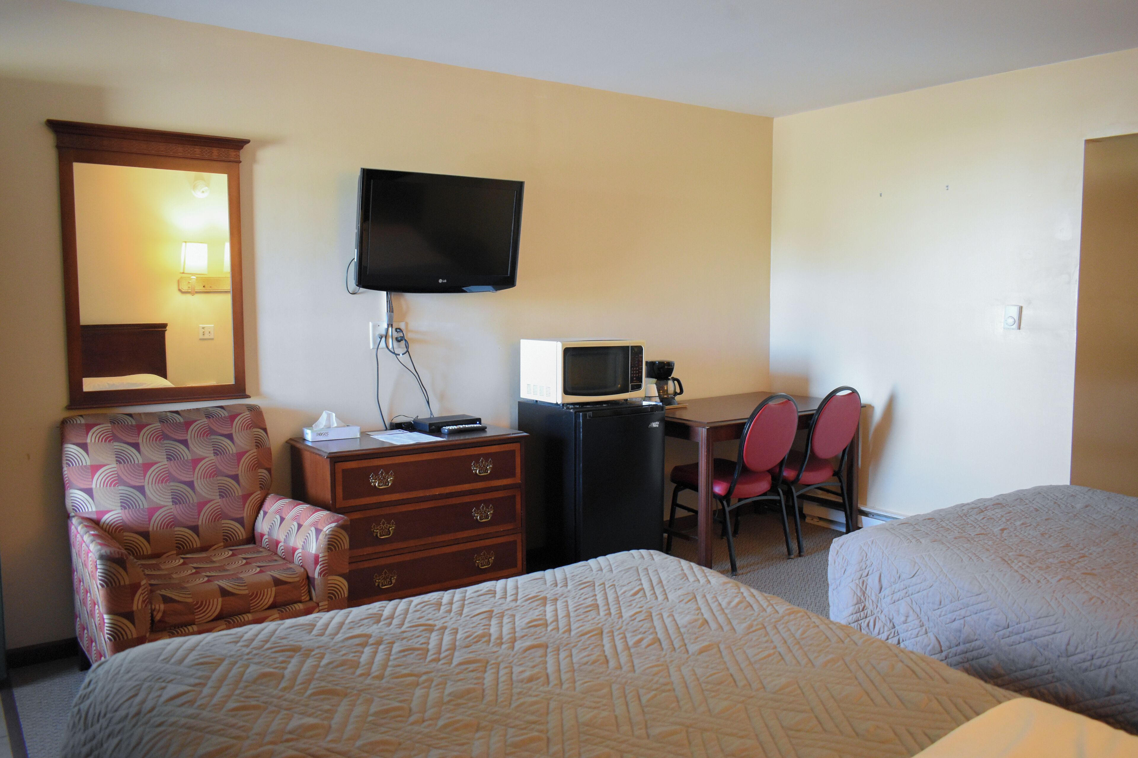 A hotel room with two beds, a desk with a chair, a television, a microwave, and a dresser.