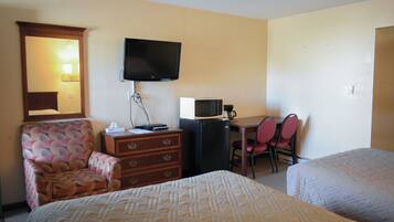 A hotel room with two beds, a desk with a chair, a television, a microwave, and a dresser.