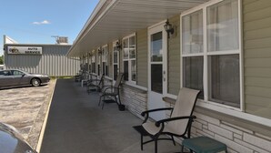 Un motel con un espacio de esparcimiento techado al aire libre, un coche estacionado afuera y un letrero que dice 'AUTO SERVICE'.