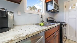 Una cocina con estufa de acero inoxidable, microondas, cafetera y ventana con vista a árboles.
