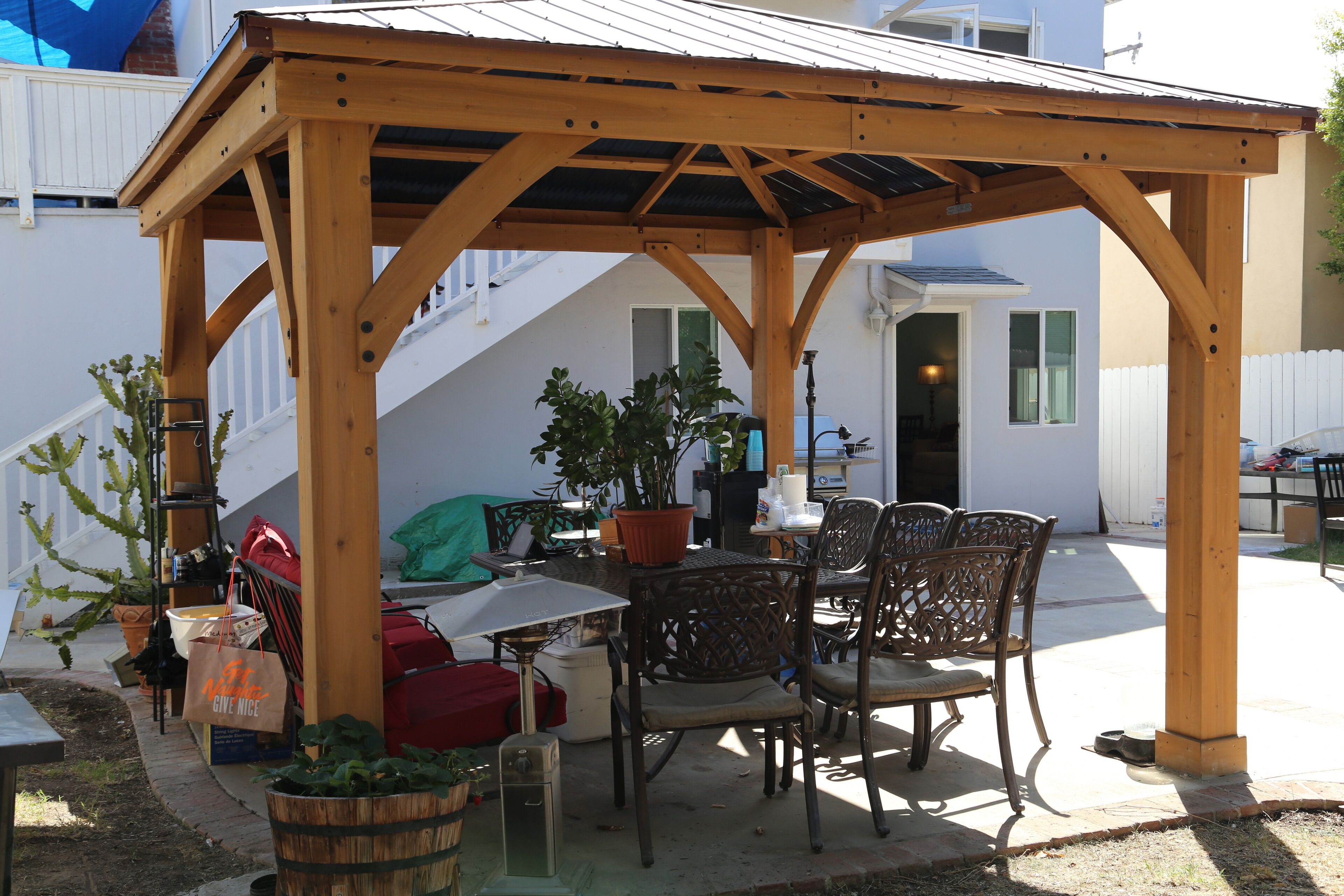 Eine Holz-Pergola mit Tisch und Stühlen, umgeben von Blumentöpfen und Gartenmöbeln.