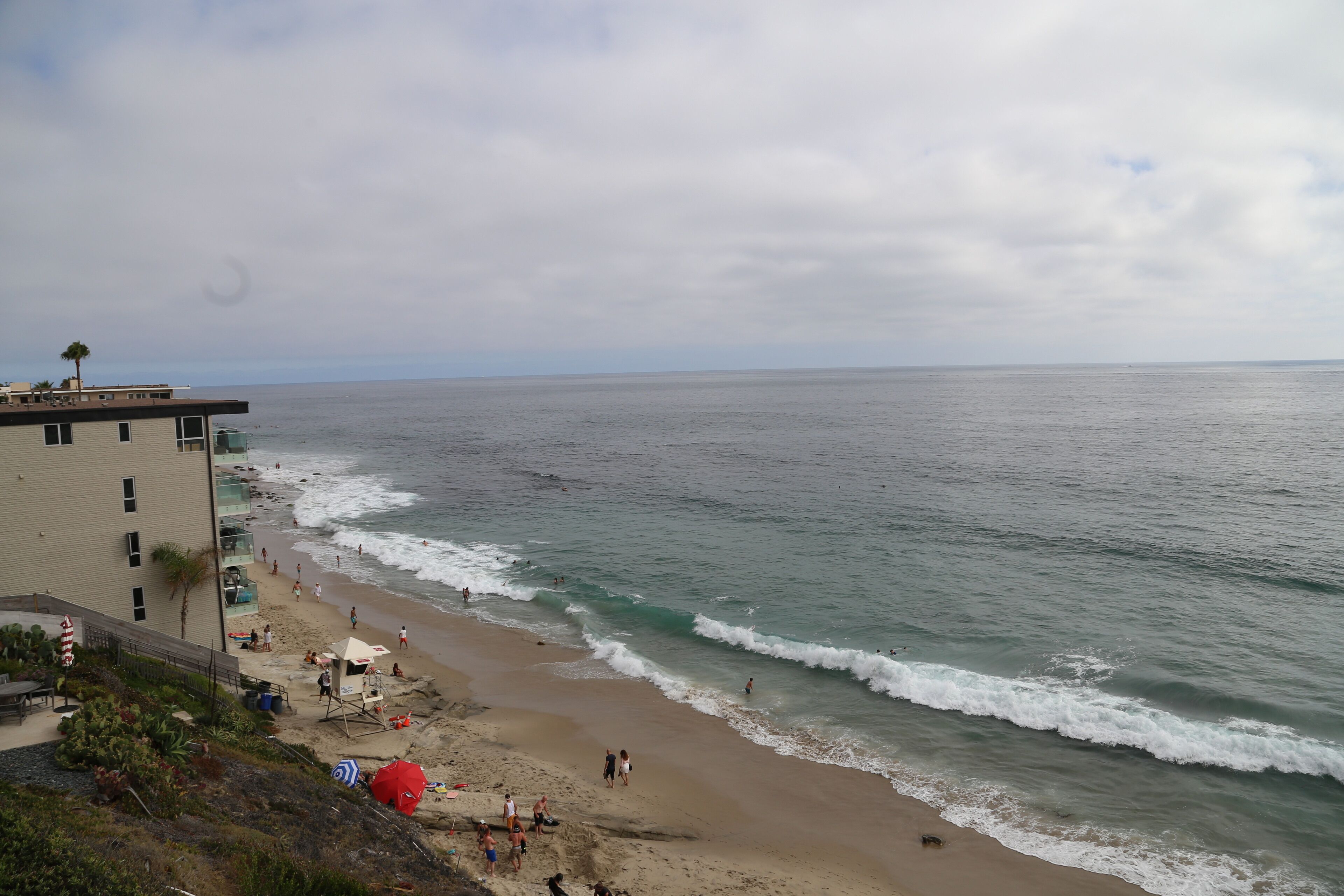 Une plage avec un bâtiment sur la gauche, des vagues qui déferlent sur le rivage et des gens qui profitent de la plage.