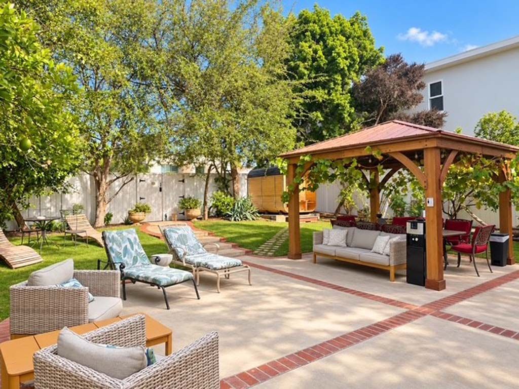 Ein Terrassenbereich im Freien mit Korbmöbeln, einer Holzpergola und einem Rasen.