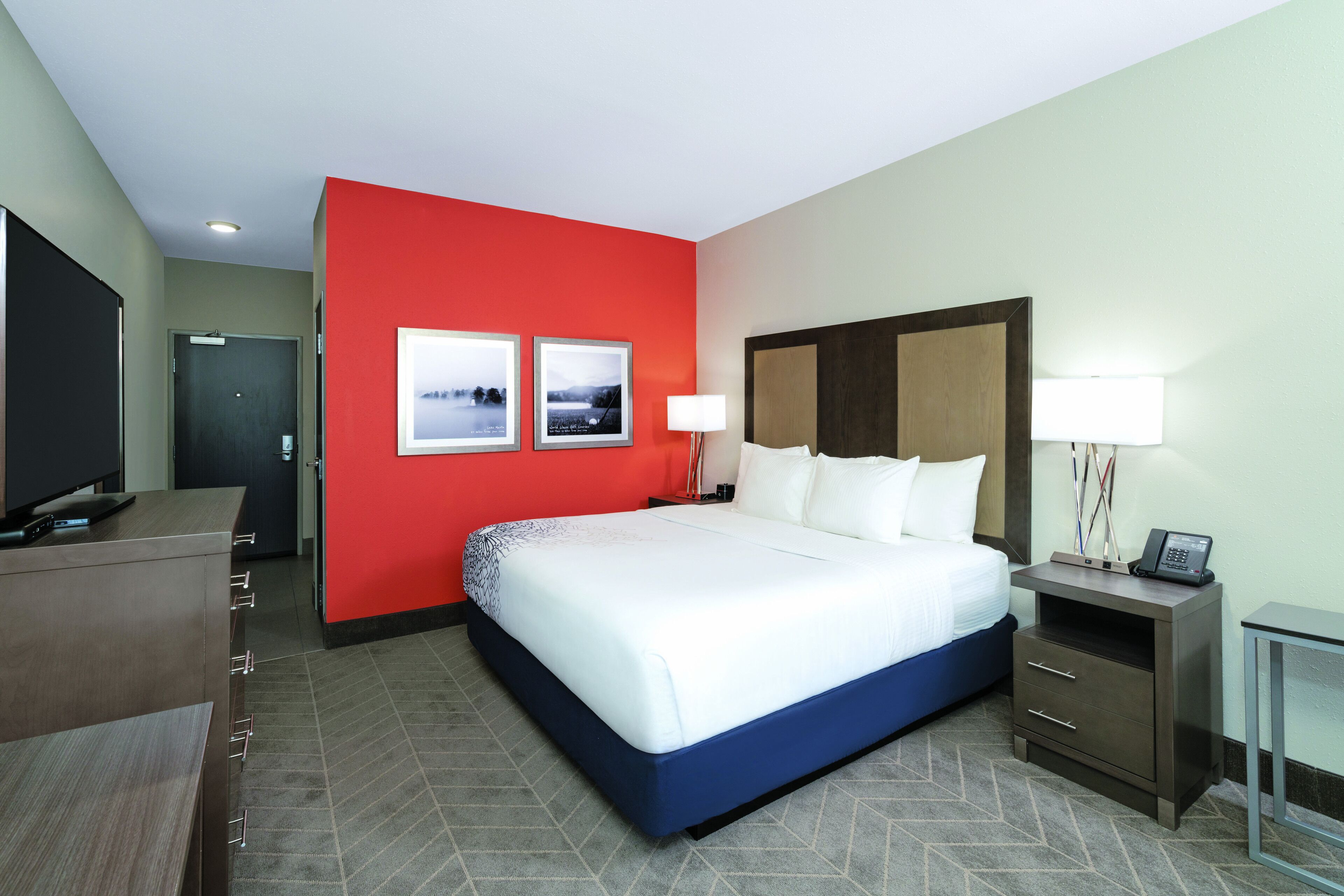 A hotel room with a large bed, a desk, a TV, and two framed pictures on the wall.