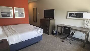 A hotel room with a bed, a desk, a chair, a TV, and two framed pictures on the wall.