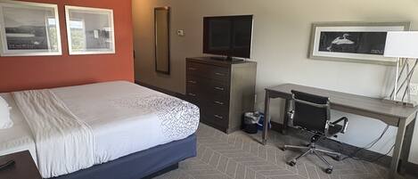 A hotel room with a bed, a desk, a chair, a TV, and two framed pictures on the wall.