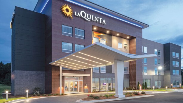 A La Quinta hotel with a modern design, featuring a prominent sun logo, a covered entrance, and a well-lit facade. - La Quinta Inn & Suites by Wyndham Opelika Auburn (Opelika)