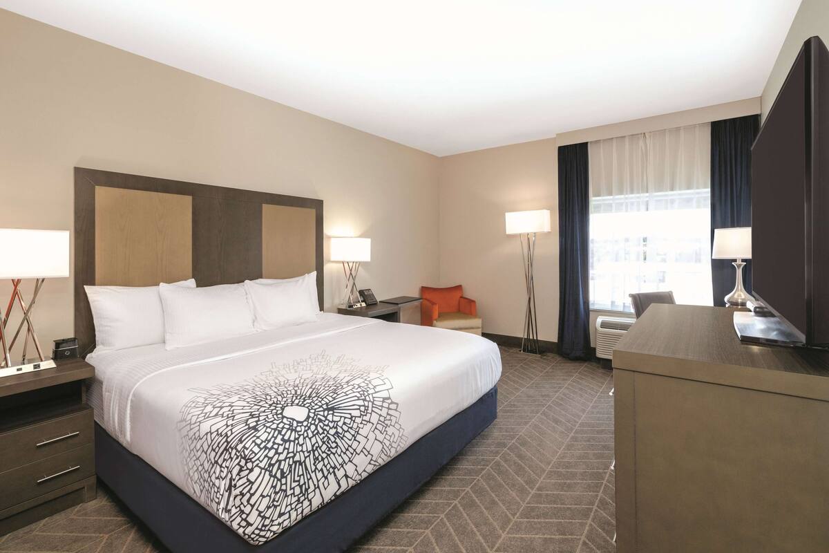 Una habitación de hotel con una cama grande, dos mesitas de noche, un escritorio, una silla y una ventana con cortinas.
