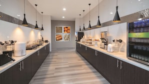 A modern kitchen with dark wood cabinets, a marble countertop, and black pendant lighting. - La Quinta Inn & Suites by Wyndham Opelika Auburn (Opelika)