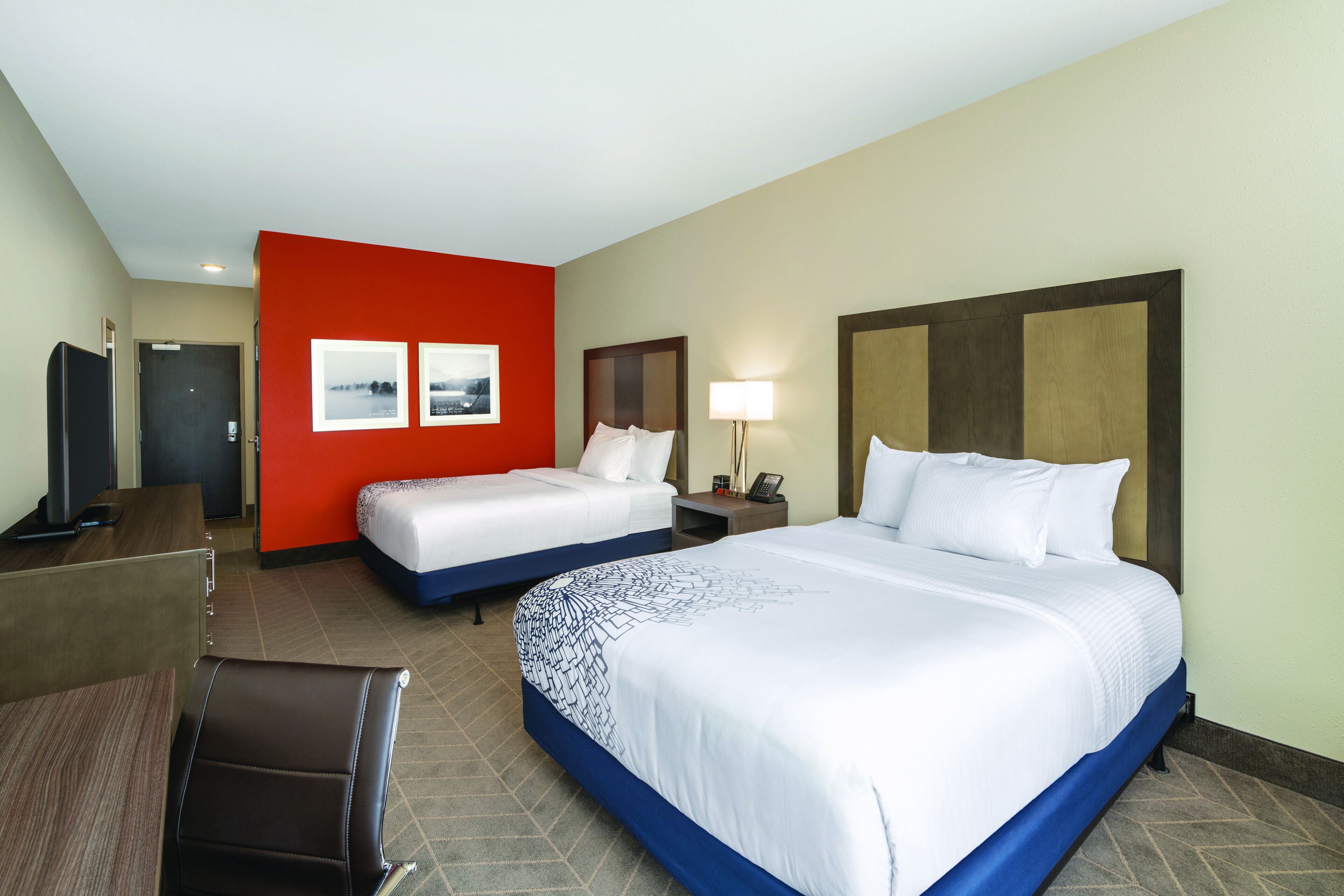 A hotel room with two beds, a desk, a chair, and a TV.