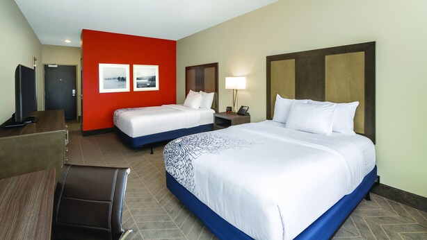 A hotel room with two beds, a desk, a chair, and a TV.