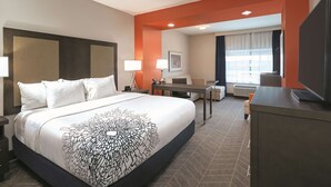 A hotel room with a large bed, a desk, a chair, a TV, and a window with curtains. - La Quinta Inn & Suites by Wyndham Opelika Auburn (Opelika)
