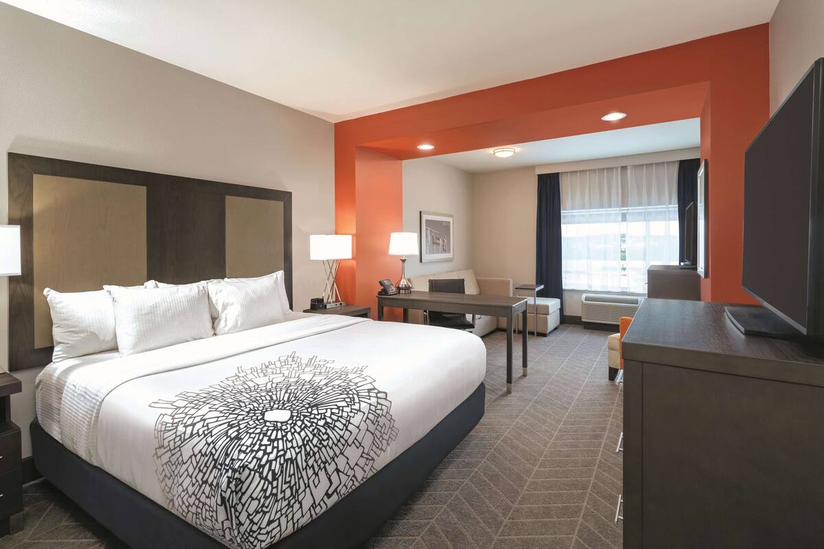 Habitación de hotel con una cama grande, un escritorio, una silla, un televisor y una ventana con cortinas.