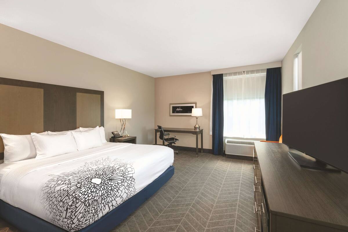 Habitación de hotel con una cama grande, un escritorio, una silla, un televisor y una ventana con cortinas.
