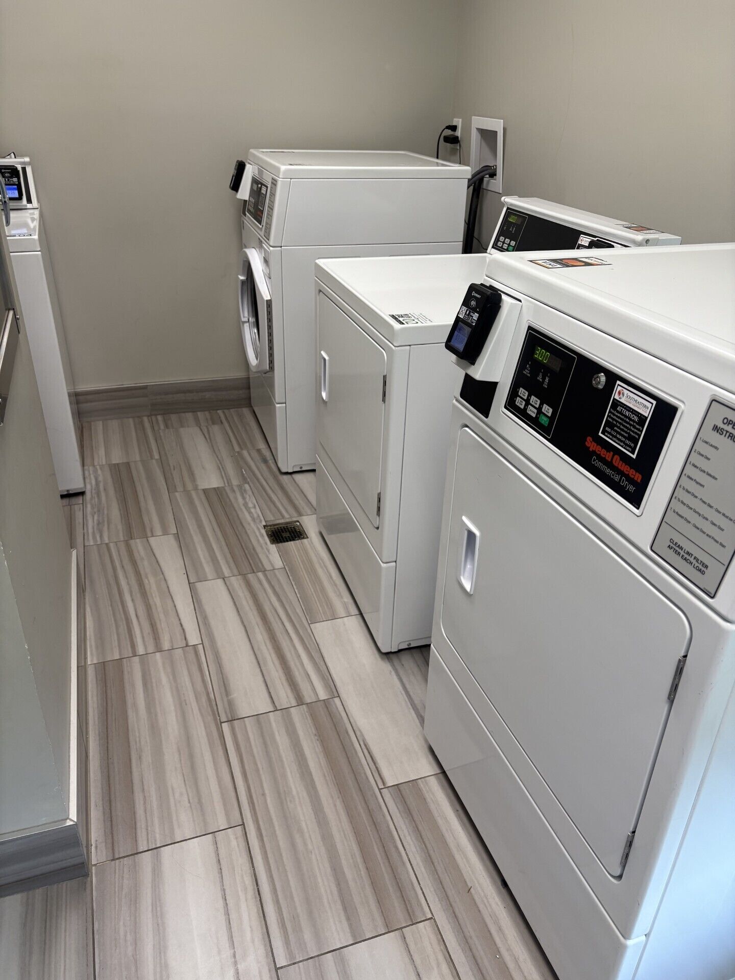 A laundry room with three stacked washers and dryers, a control panel, and a tiled floor.