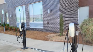 A parking area with electric vehicle charging stations, a building with a brick facade, and a clear sky.