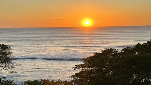 Ein Sonnenuntergang über dem Meer mit Wellen und Bäumen im Vordergrund.
