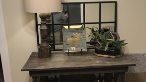A rustic wooden table with a lamp, a deer painting, and a potted plant. - The Wilson House  Beautiful Downtown Murfreesboro Cottage Close to MTSU / I 24 (Murfreesboro)