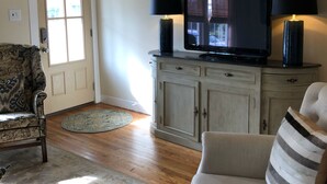A living room with a sofa, a television, and two lamps. There is a door and a rug on the floor. - The Wilson House  Beautiful Downtown Murfreesboro Cottage Close to MTSU / I 24 (Murfreesboro)