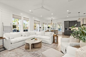 Ein geräumiges Wohnzimmer mit einem großen, weißen Ecksofa, einem runden Couchtisch und einer Küche im Hintergrund.